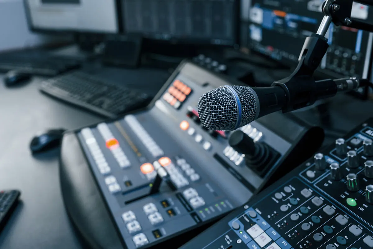 A hand on the faders of a radio studio mixing console